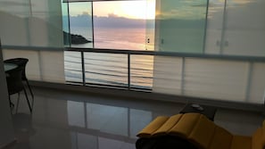 A room with a large window overlooking a body of water and distant land, a small table, and a yellow chair.