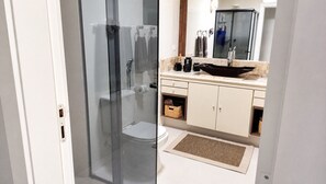 Moderni kylpyhuone, jossa on lasinen suihkuseinä, wc-istuin, mustalla altaalla varustettu pesuallas ja peili pesualtaan yläpuolella.