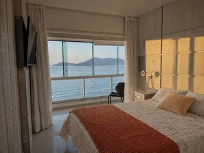 A bedroom with a large window, a bed, a chair, and a nightstand.