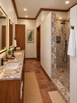 Un baño con tocador doble, ducha con azulejos estampados y puerta de madera.