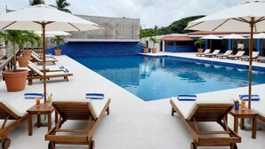 A pool area with lounge chairs and umbrellas, surrounded by a tiled deck and palm trees.