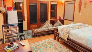 A room with a bed, a wooden bench, a table with books, a refrigerator, and a window.