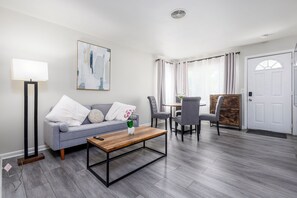 Ein modernes Wohnzimmer mit grauem Sofa, Couchtisch und einem Essbereich mit Stühlen und Tisch.