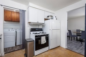 Una cocina compacta con estufa a gas, horno empotrado, refrigerador y lavadora.