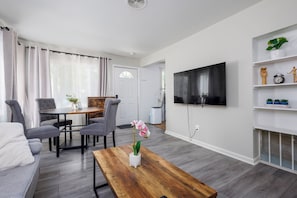 A modern living room with a flat-screen TV, a dining area with a table and chairs, and a small bookshelf with decorative items. - 3/1 Home in Southfield, Near Hospitals & Parks (Southfield)
