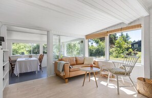 A sunlit room with a sofa, a round table, and a dining table with chairs.