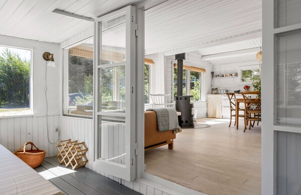 A spacious room with a large window, a sofa, a dining table, and a kitchen area.