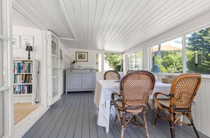 A covered outdoor dining area with a table and chairs, a bookshelf, and a cabinet. - Idyllic holiday home with large garden (Fårevejle)