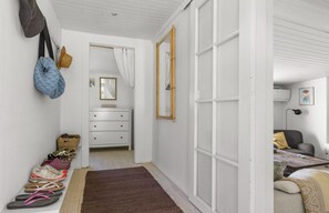 A room with a white dresser, a mirror, a brown rug, and a door leading to another room. - Idyllic holiday home with large garden (Fårevejle)
