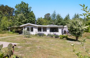 A single-story house with a covered porch, surrounded by a grassy yard and trees. - Idyllic holiday home with large garden (Fårevejle)