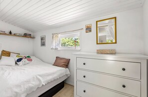 A bedroom with a bed, a dresser, a window with curtains, and a mirror. - Idyllic holiday home with large garden (Fårevejle)