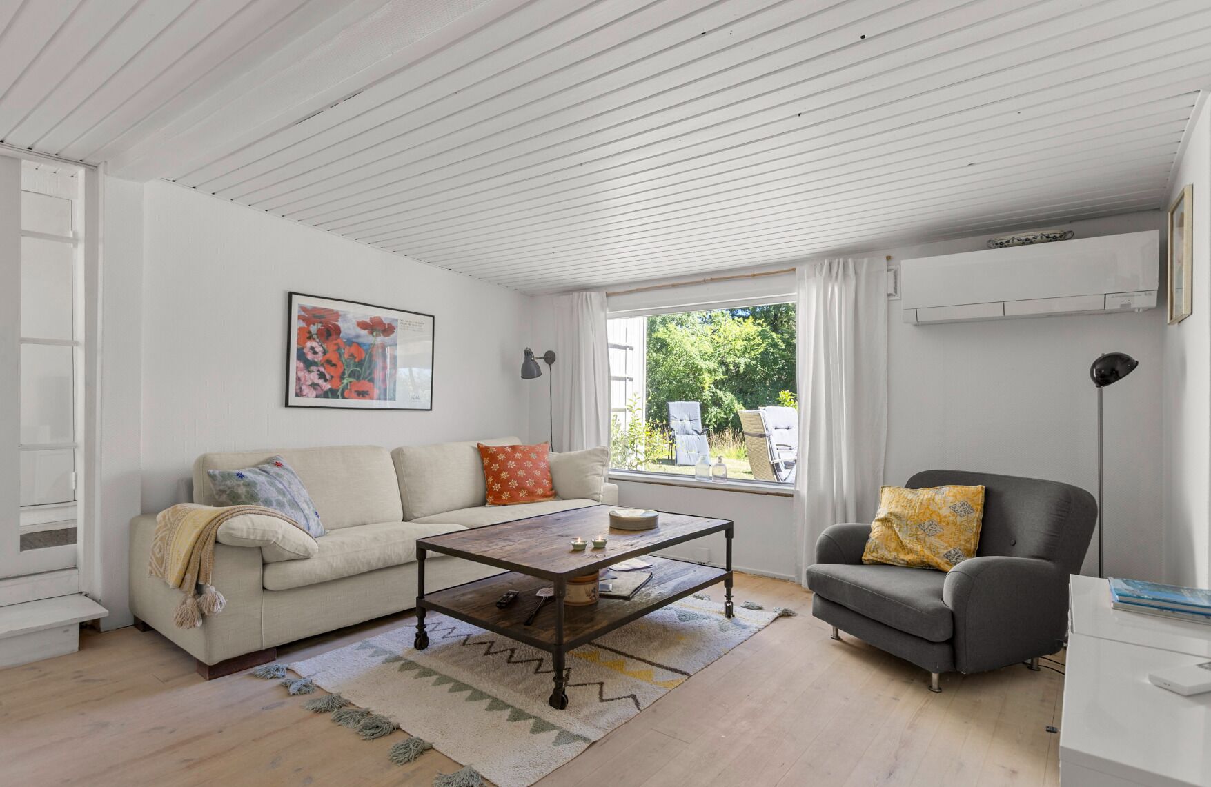 Una sala de estar con sofá, sillón, mesa de centro y ventana con vista a la vegetación.