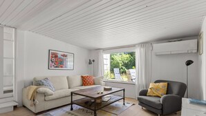 En stue med sofa, lænestol, sofabord og et vindue med udsigt til grønne omgivelser.