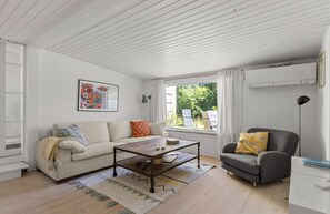 A living room with a sofa, armchair, coffee table, and a window with a view of greenery outside. - Idyllic holiday home with large garden (Fårevejle)