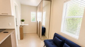 A modern living room with a sofa, a small kitchen area, and a large window providing natural light. - Charming studio at midtown (Miami)
