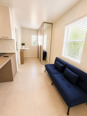 A modern living room with a sofa, a small kitchen area, and a large window providing natural light. - Charming studio at midtown (Miami)