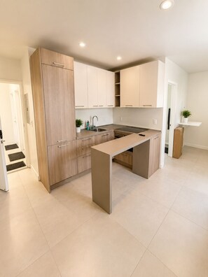 A modern kitchen with light wood cabinetry, a central island, and a built-in stove. - Charming studio at midtown (Miami)