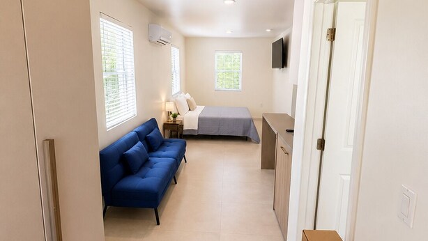 A compact hotel room with a bed, a blue sofa, a small table, and a TV. - Charming studio at midtown (Miami)