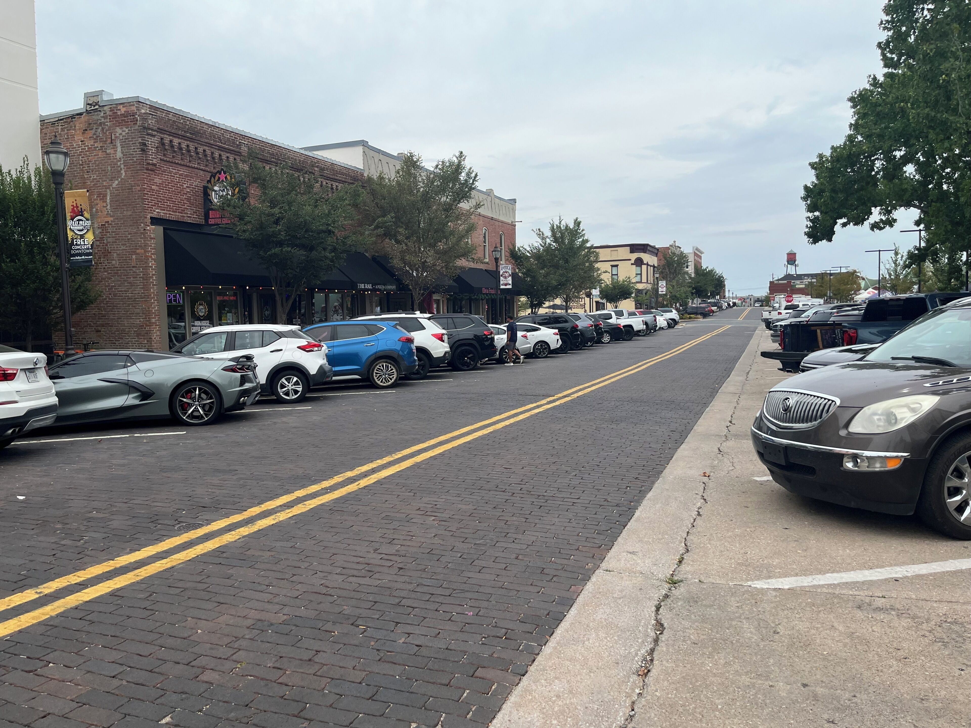 Rua com carros estacionados e edifícios com lojas.