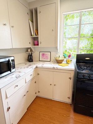 A kitchen with white cabinets, a microwave, a stove, and a window with a view of greenery.