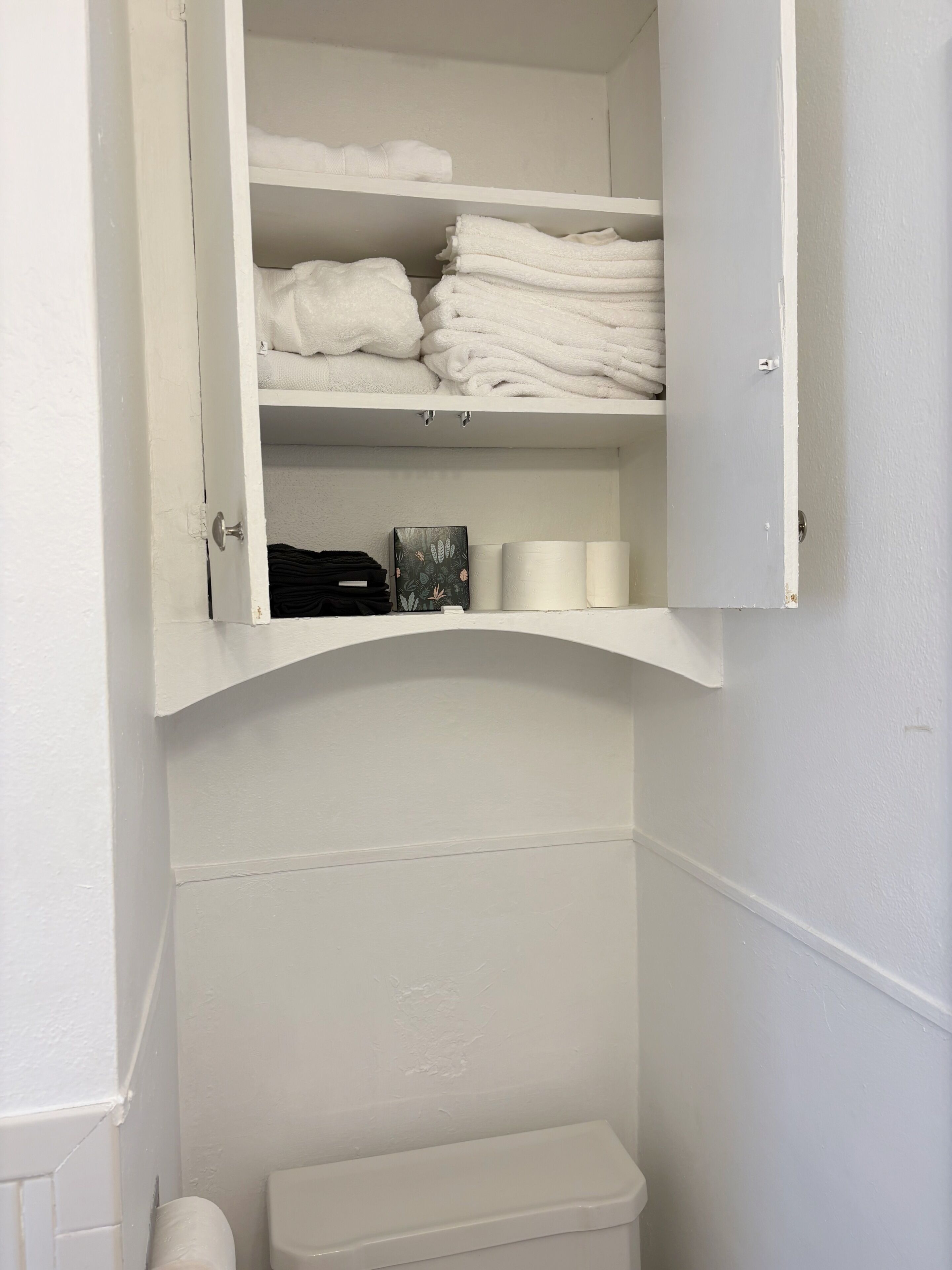 A white bathroom with a cabinet containing folded towels and toiletries.