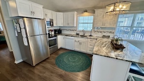 A modern kitchen with white cabinetry, stainless steel appliances, and a green rug. - Ocean Lakes Ocean View Beach House | 4th House From Beach | Golf Cart | Sleeps 8 (Myrtle Beach)