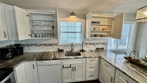 A kitchen with white cabinets, a marble countertop, a built-in sink, and a window with blinds. - Ocean Views, Ocean Breeze and the Sound of Waves (Myrtle Beach)
