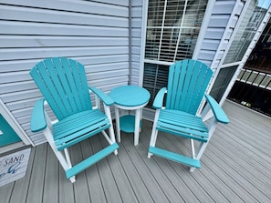 Um deck de madeira com duas cadeiras Adirondack turquesa e uma pequena mesa redonda.
