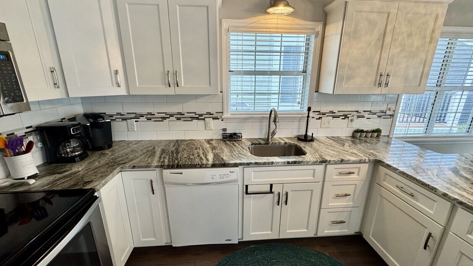 A kitchen with white cabinets, a granite countertop, a dishwasher, and a window with blinds.
