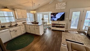 A spacious living area with a kitchen, a large flat-screen TV, and a sliding glass door leading to a balcony. - Ocean Views, Ocean Breeze and the Sound of Waves (Myrtle Beach)
