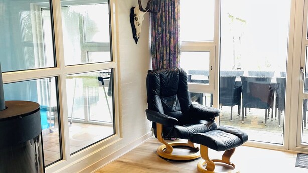 Une pièce dotée d’une grande fenêtre, d’un fauteuil en cuir noir et d’un plancher en bois.