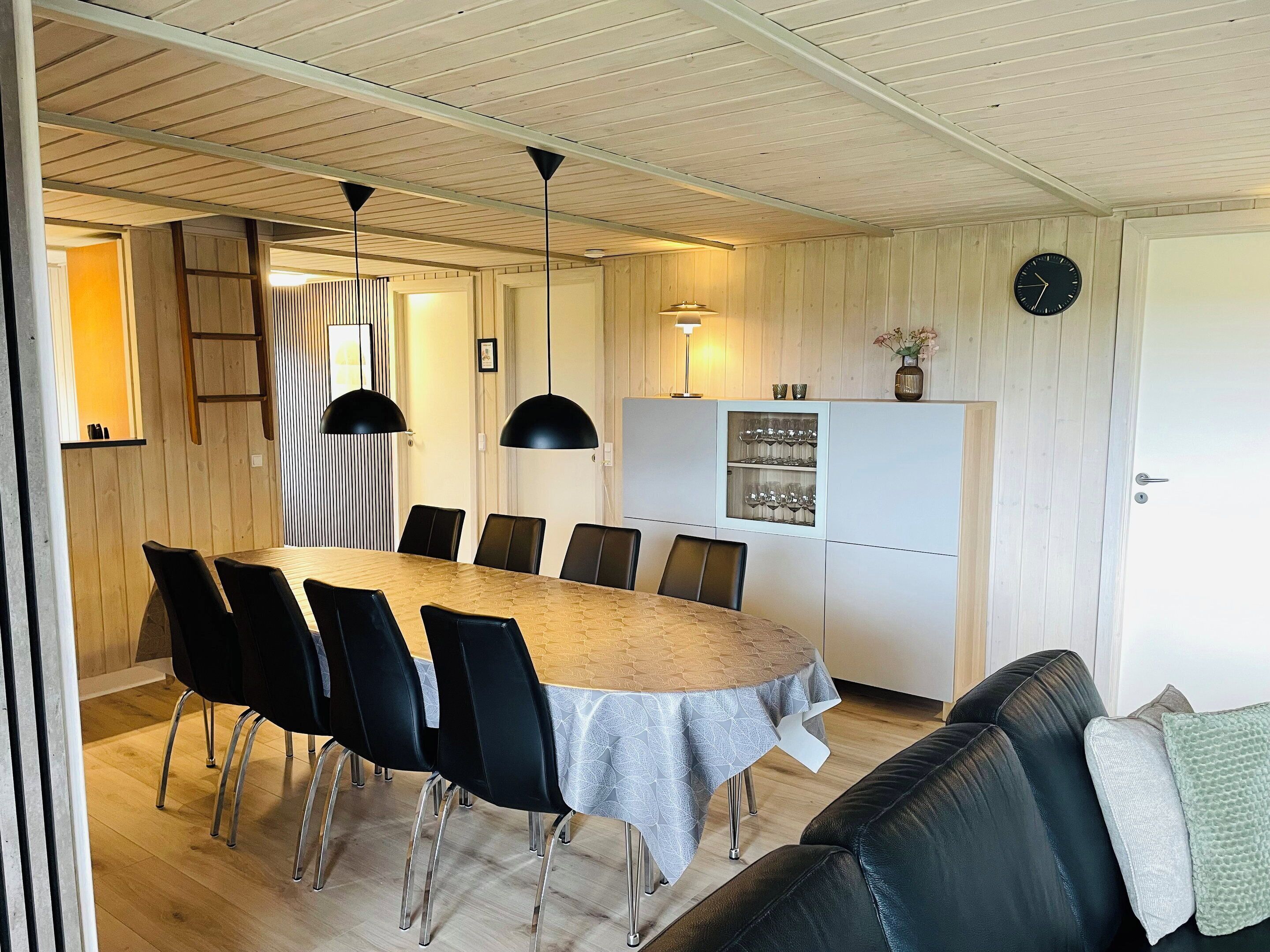 Un comedor con una mesa redonda, sillas negras y un armario blanco con cristalería.