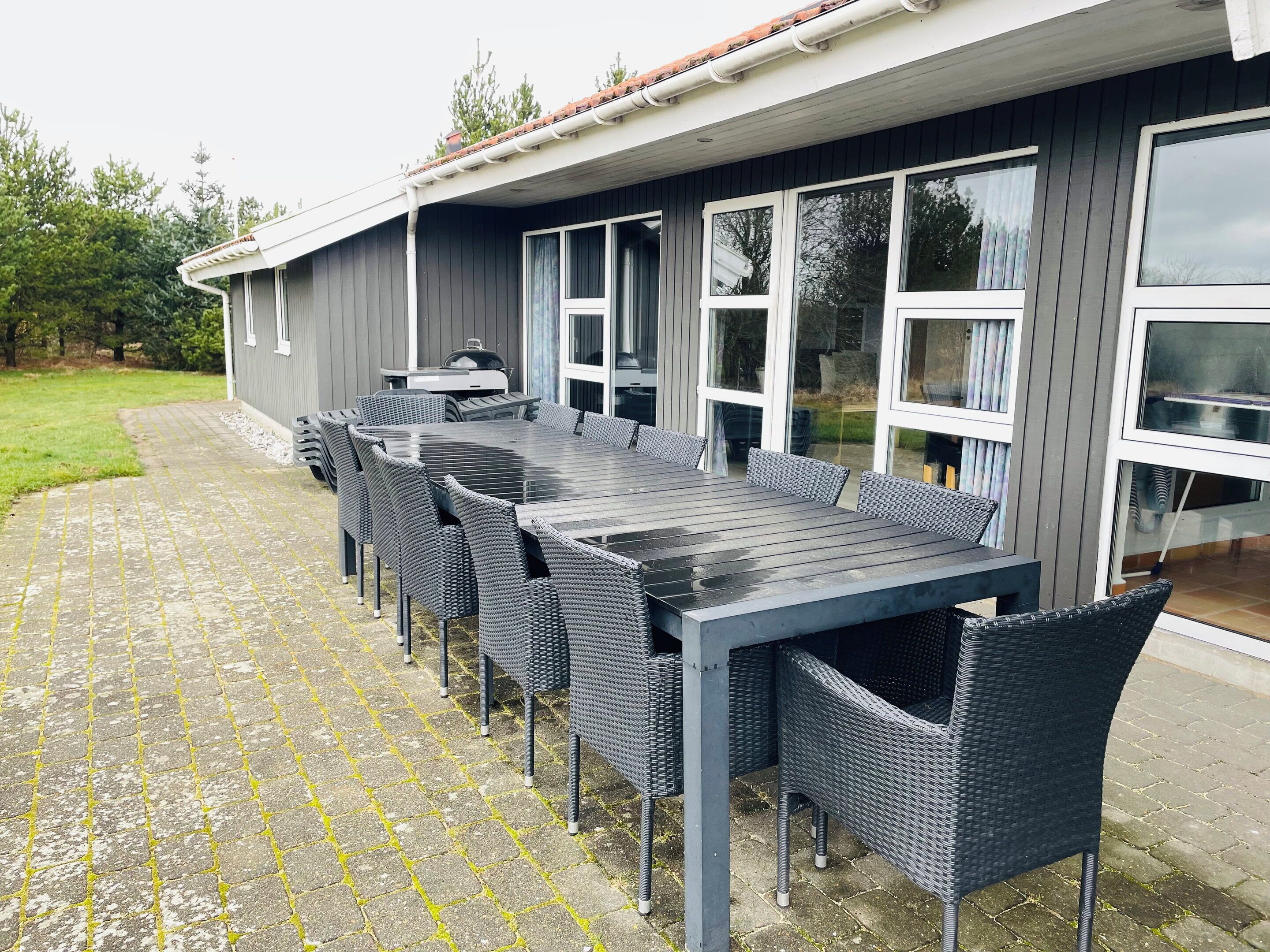 Ein Essbereich im Freien mit einem langen Tisch, Stühlen, einem Grill und einer überdachten Terrasse.