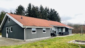 Un bâtiment à deux étages, doté d’un toit recouvert de tuiles rouges, d’un espace extérieur aménagé avec des sièges et d’une pelouse verdoyante.