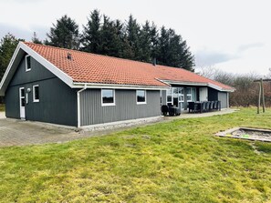 A two-story building with a red-tiled roof, a covered outdoor seating area, and a grassy lawn. - Spacious holiday home in West Jutland (Nørre Nebel)