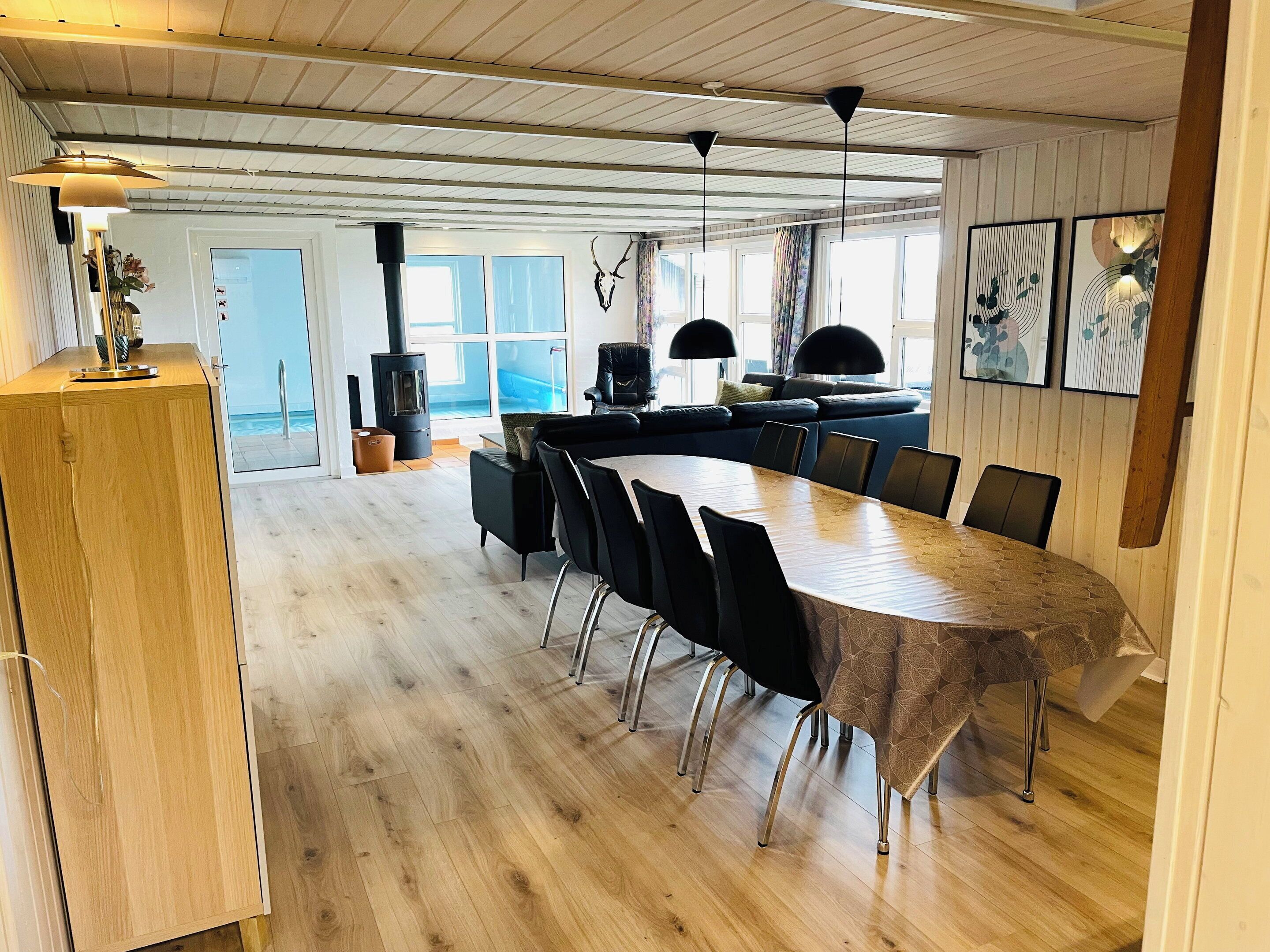 A spacious dining area with a long table and chairs, a wooden ceiling, and a view through large windows.
