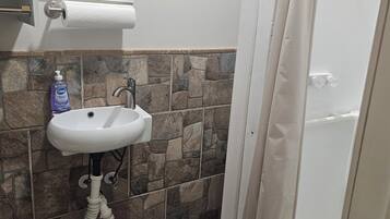 Une salle de bain avec un lavabo blanc, un miroir, un rideau de douche et une poubelle.