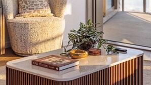 A modern living room with a sofa, a coffee table with a book, a plant, and a remote control. - "MAIN VIEW" By TheGuestHouse. (Main Beach)