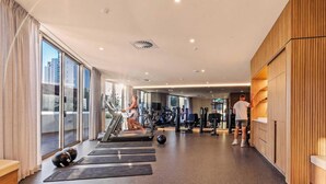 A gym with exercise equipment, a treadmill, and a person using a rowing machine. - "MAIN VIEW" By TheGuestHouse. (Main Beach)