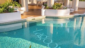 A clear swimming pool with a tiled edge, surrounded by white planters with greenery, and outdoor seating areas with chairs. - "MAIN VIEW" By TheGuestHouse. (Main Beach)