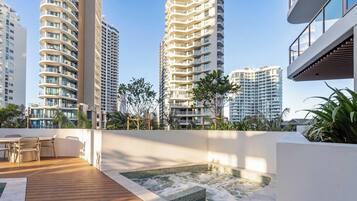 A rooftop terrace with a hot tub, outdoor seating, and views of high-rise buildings.