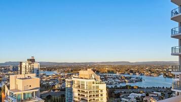 A high-rise building with multiple balconies overlooking a coastal cityscape with a river and distant hills.