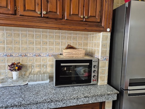 A kitchen with a built-in toaster oven, a stainless steel refrigerator, and a tiled backsplash.