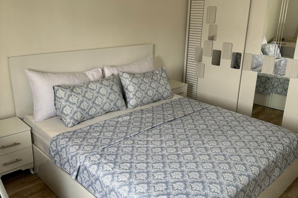 Un lit avec une couvre-lit à motifs et des oreillers, une table de chevet avec des tiroirs et une armoire avec des portes miroir et une tringle pour suspendre les vêtements.