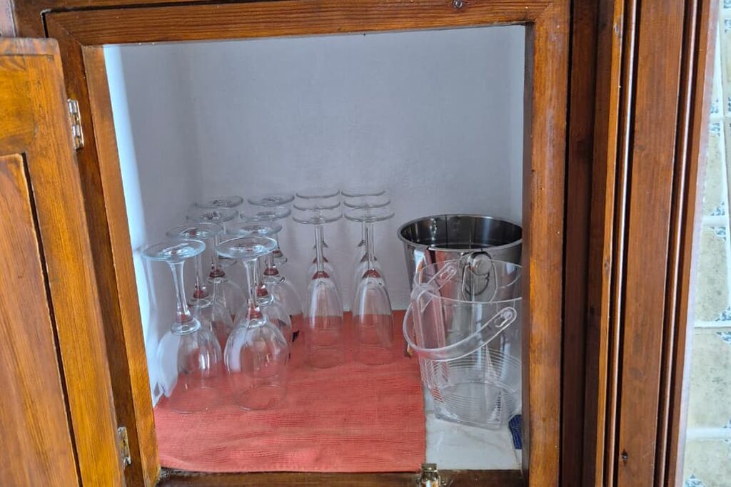 Un mueble de madera con un paño rojo, que contiene varios vasos de vino y un recipiente metálico.