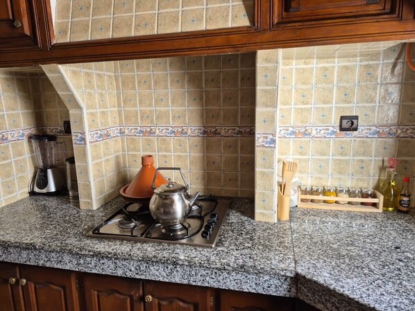 A kitchen with a gas stove, a blender, a kettle, and a spice rack.