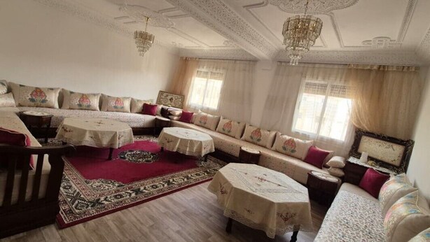 A spacious living room with a sofa set, two round tables, and a patterned rug. - Confort plus (Agadir)