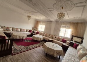 A spacious living room with a sofa set, two round tables, and a patterned rug.