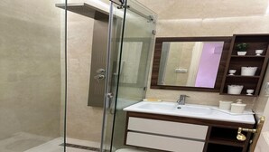 A bathroom with a glass-enclosed shower, a white sink, a wooden vanity, and a mirror above the sink. - Confort plus (Agadir)