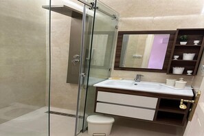 Ein Badezimmer mit einer gläsernen Duschkabine, einem weißen Waschbecken, einem Holz-Waschtisch und einem Spiegel über dem Waschbecken.